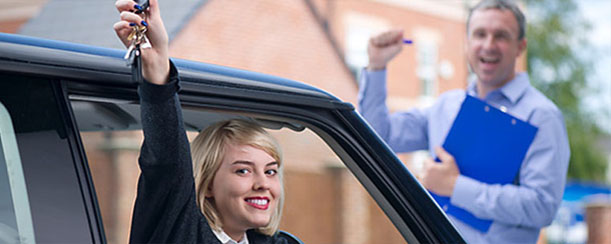 Young student sitting in driver's seat is smiling and holding Car keys up in the air as the instructor cheers.